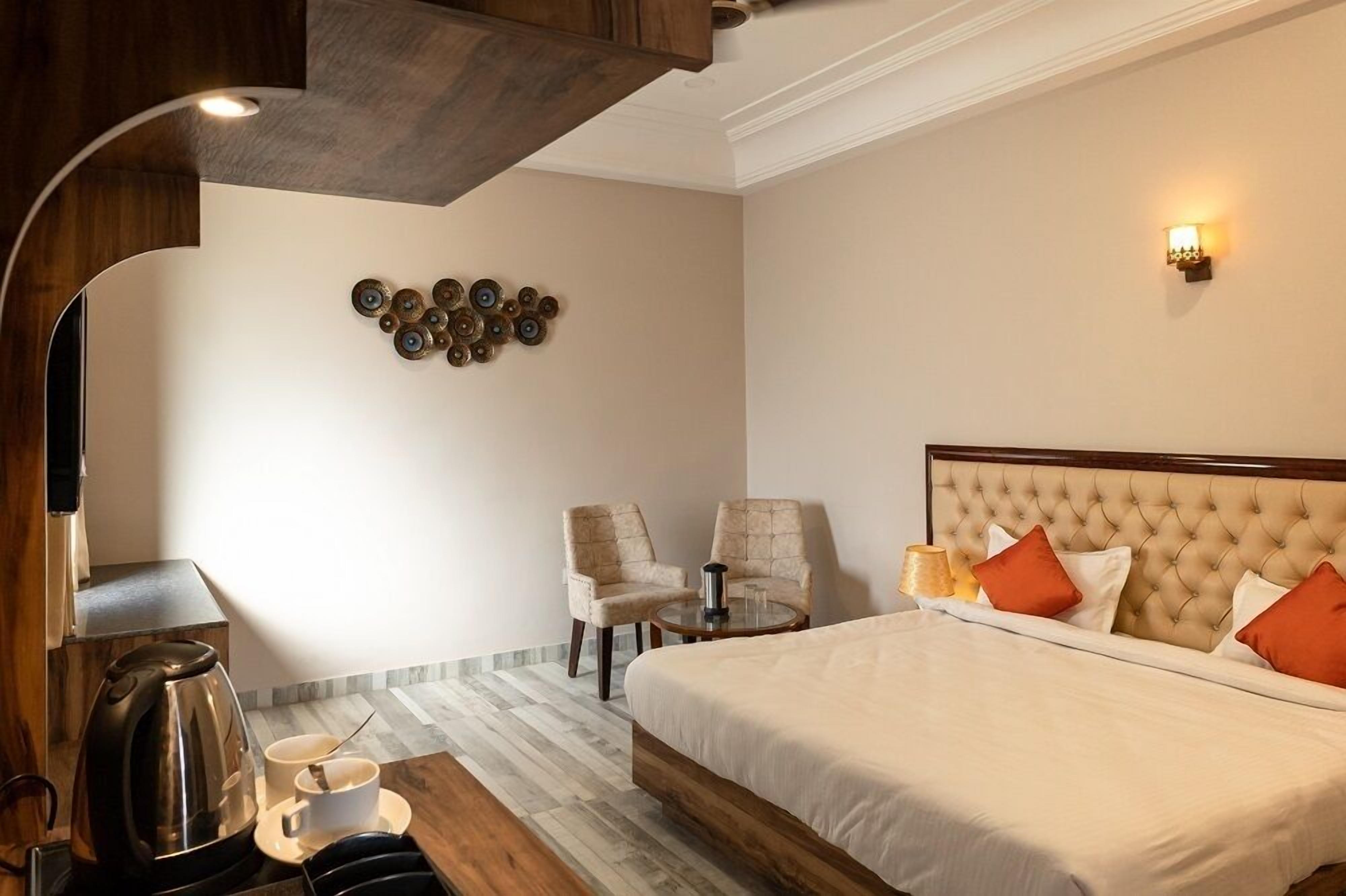 A hotel room with a bed, two chairs, a coffee table, a coffee maker, and a wall art piece.