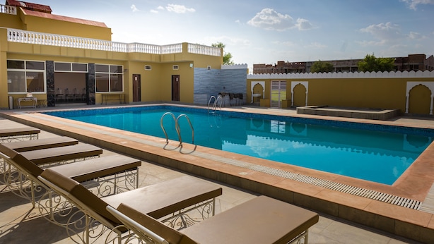 A swimming pool with lounge chairs and a building with a yellow facade and white balcony.