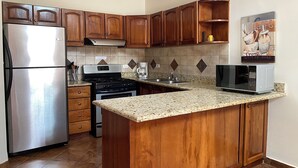 Una cocina con armarios de madera, un refrigerador de acero inoxidable, estufa, microondas y cafetera.