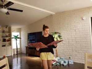 Iemand houdt een boek vast in een kamer met een baksteenmuur, een houten vloer en een televisie op een standaard.