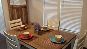 Una mesa de comedor con cuatro tazones, dos sillas, un aparador de madera y una ventana con persianas.