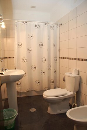 Un baño con cortina de ducha que lleva logotipos de 'H2O', un lavabo blanco, un inodoro y un cubo de basura.
