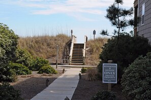 A private property entrance with a wooden staircase leading up to a gated area, surrounded by landscaped gardens and a clear sky.