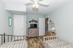 A bedroom with two beds, a ceiling fan, a dresser, a television, and a door leading to another room.