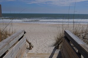 A wooden boardwalk leading to a sandy beach with the ocean in the background.
