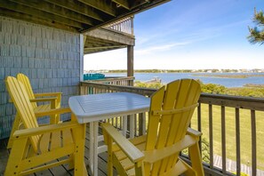 A wooden deck with a table and two chairs, overlooking a body of water with a distant shoreline. - Island In The Sun - 3BR Townhouse with Ocean & Sound Views! (North Topsail Beach)