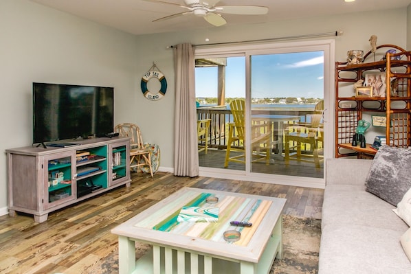 A living room with a television, a coffee table, a sofa, and a view of the outdoors through a sliding glass door.
