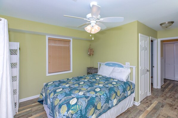 A bedroom with a bed, a ceiling fan, a window with blinds, a door, and a wooden floor. - Island In The Sun - 3BR Townhouse with Ocean & Sound Views! (North Topsail Beach)