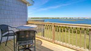 A wooden deck with a table and chairs, overlooking a body of water with a distant shoreline. - Island In The Sun - 3BR Townhouse with Ocean & Sound Views! (North Topsail Beach)