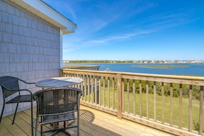 A wooden deck with a table and chairs, overlooking a body of water with a distant shoreline. - Island In The Sun - 3BR Townhouse with Ocean & Sound Views! (North Topsail Beach)