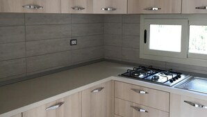 Une cuisine moderne avec des meubles de couleur bois clair, une cuisinière à gaz et une fenêtre qui laisse entrer la lumière naturelle.
