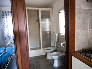 Een badkamer met twee toiletten, een toiletbrons, een douche en een wastafel.