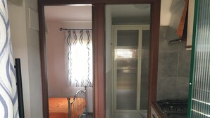 Un couloir étroit mène à une chambre comprenant un lit, un coin cuisine et une salle de bain avec douche.