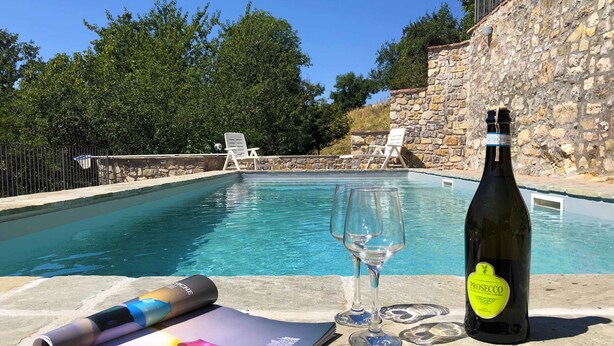 Een zwembadterras met een stenen muur, ligbedden, een fles Prosecco en een tijdschrift.