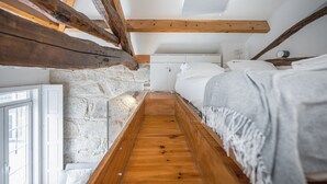 Un dormitorio bajo en ático con vigas de madera a la vista, una pared de piedra y suelo de madera.