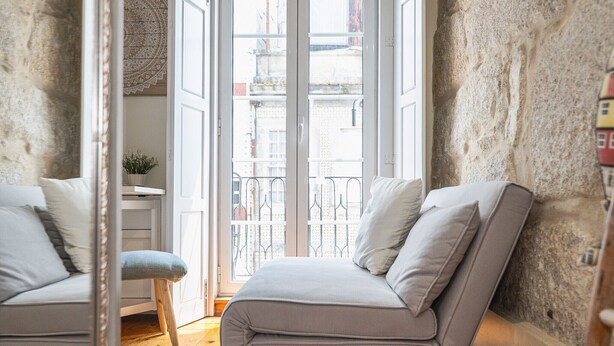 Una habitación con sofá, una silla, una mesita con una planta y vistas a través de un ventanal.