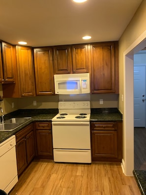 A kitchen with wooden cabinets, a white stove, a microwave, and a granite countertop.