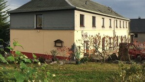 A two-story building with a sloped roof, a small porch, and a garden area with various plants. - Landhotel Elterlein (Elterlein)