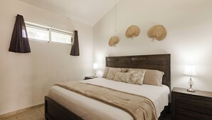 Un dormitorio con una cama grande, dos mesitas de noche con lámparas, una ventana con cortinas y tres objetos decorativos colgados en la pared.
