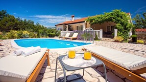 Un espace piscine avec des chaises longues, une table avec des boissons et une maison en arrière-plan.