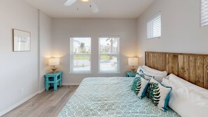 A bedroom with a large bed, two bedside tables with lamps, a wooden headboard, and a window with blinds. - Golf Cart Included, Shared Pool, Hot Tub, Boardwalk to Beach, Pet Friendly (Port Aransas)
