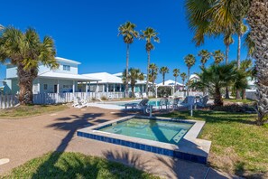 A pool area with two pools, palm trees, and a building with a white fence. - Golf Cart Included, Shared Pool, Hot Tub, Boardwalk to Beach, Pet Friendly (Port Aransas)