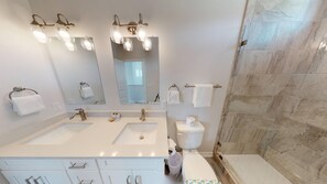 A modern bathroom with two sinks, a large mirror, and a shower area. - Golf Cart Included, Shared Pool, Hot Tub, Boardwalk to Beach, Pet Friendly (Port Aransas)