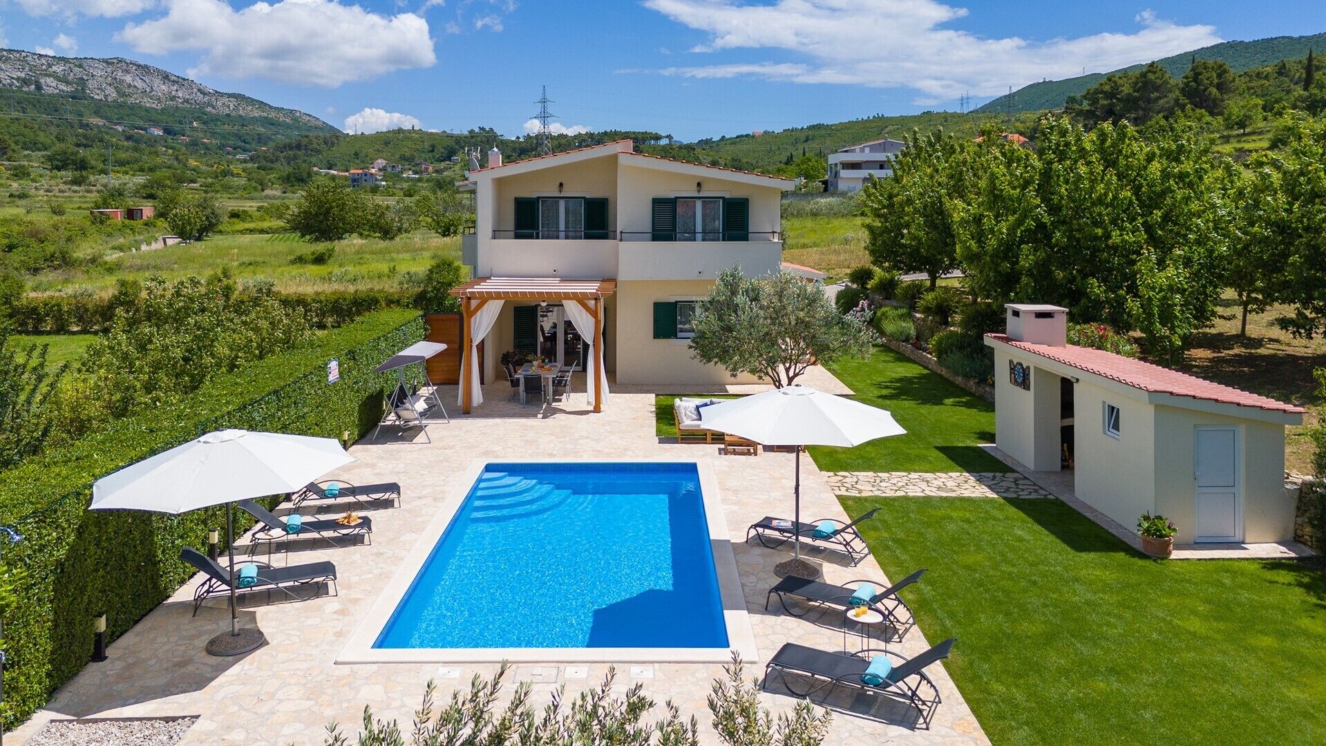 Una casa de dos pisos con piscina, mobiliario exterior y jardín.