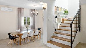 A modern dining area with a glass table and chairs, a chandelier, and a staircase with wooden steps and a black railing. - VILLA ROKO with 4 bedrooms, 32sqm heated pool, playground (Tugare)