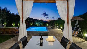 An outdoor dining area with a table, chairs, a bottle of wine, and candles. A pool is visible in the background. - VILLA ROKO with 4 bedrooms, 32sqm heated pool, playground (Tugare)