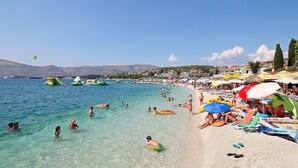 Una playa con aguas cristalinas, gente nadando y tomando el sol, y sombrillas de colores.