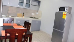 A compact kitchen with grey cabinets, a wooden dining table, and a stainless steel refrigerator. - Kadny Court by Citi Apartments (Dansoman)
