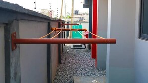 A narrow outdoor corridor with a metal horizontal bar structure, gravel ground, and buildings in the background. - Kadny Court by Citi Apartments (Dansoman)