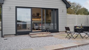 A modern house with a large sliding glass door leading to a living area with a sofa and a dining table. - 1 bedroom accommodation in Balcary, near Auchencairn (Balcary, near Auchencairn)