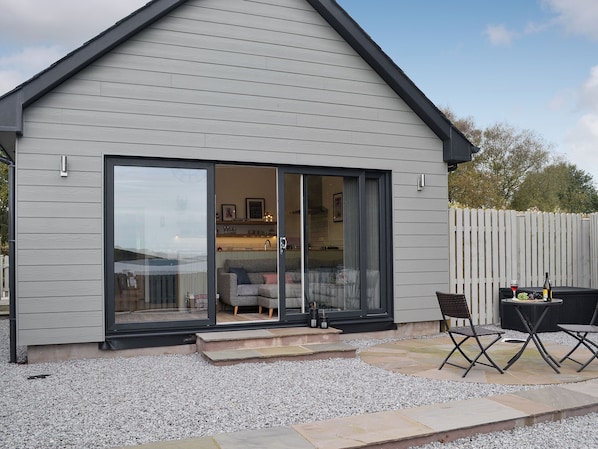A modern house with a large sliding glass door leading to a living area with a sofa and a dining table. - 1 bedroom accommodation in Balcary, near Auchencairn (Balcary, near Auchencairn)