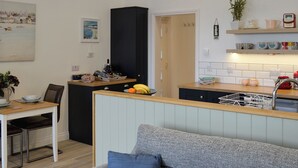 A compact kitchen with a dining area, a black cabinet, and a clock on the wall. - 1 bedroom accommodation in Balcary, near Auchencairn (Balcary, near Auchencairn)