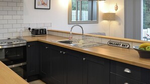 A kitchen with a stainless steel range hood, a built-in oven, a sink with a dish rack, and a wooden countertop. - 1 bedroom accommodation in Balcary, near Auchencairn (Balcary, near Auchencairn)