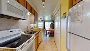 A kitchen with a microwave, stove, sink, and refrigerator. There is a dining area with a table and chairs. - Walk to Sandfest, Shared Pools, Boardwalk to the Beach (Port Aransas)