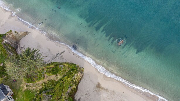 Vista aérea de una playa con aguas turquesas cristalinas, orilla arenosa y afloramientos rocosos.