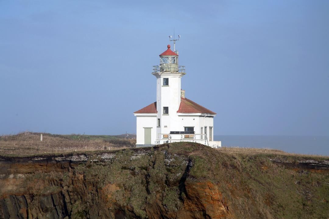 Un phare blanc, surmonté d’un toit rouge, se dresse sur une falaise rocheuse.