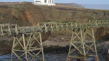 A white lighthouse with a red roof on a cliff overlooking the sea, with a wooden bridge in the foreground.