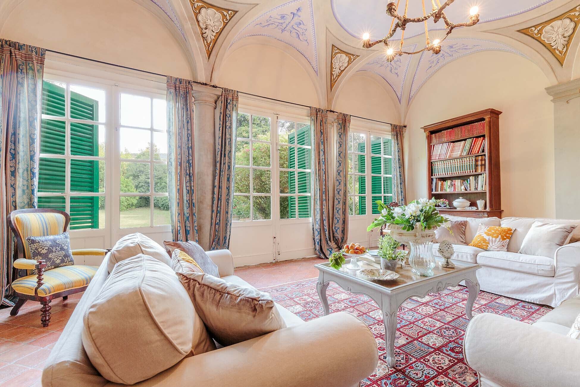 A spacious living room with a large window, a bookshelf, and a chandelier.