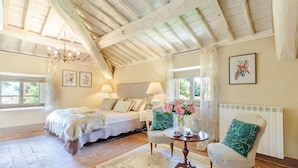 Un dormitorio amplio con una cama grande, una cama más pequeña, una mesa redonda con un jarrón de flores y una silla con un cojín verde.