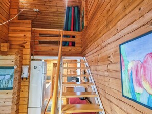 L’intérieur d’une cabane en bois comprend un coin cuisine, une échelle menant à une mezzanine et un tableau accroché au mur.