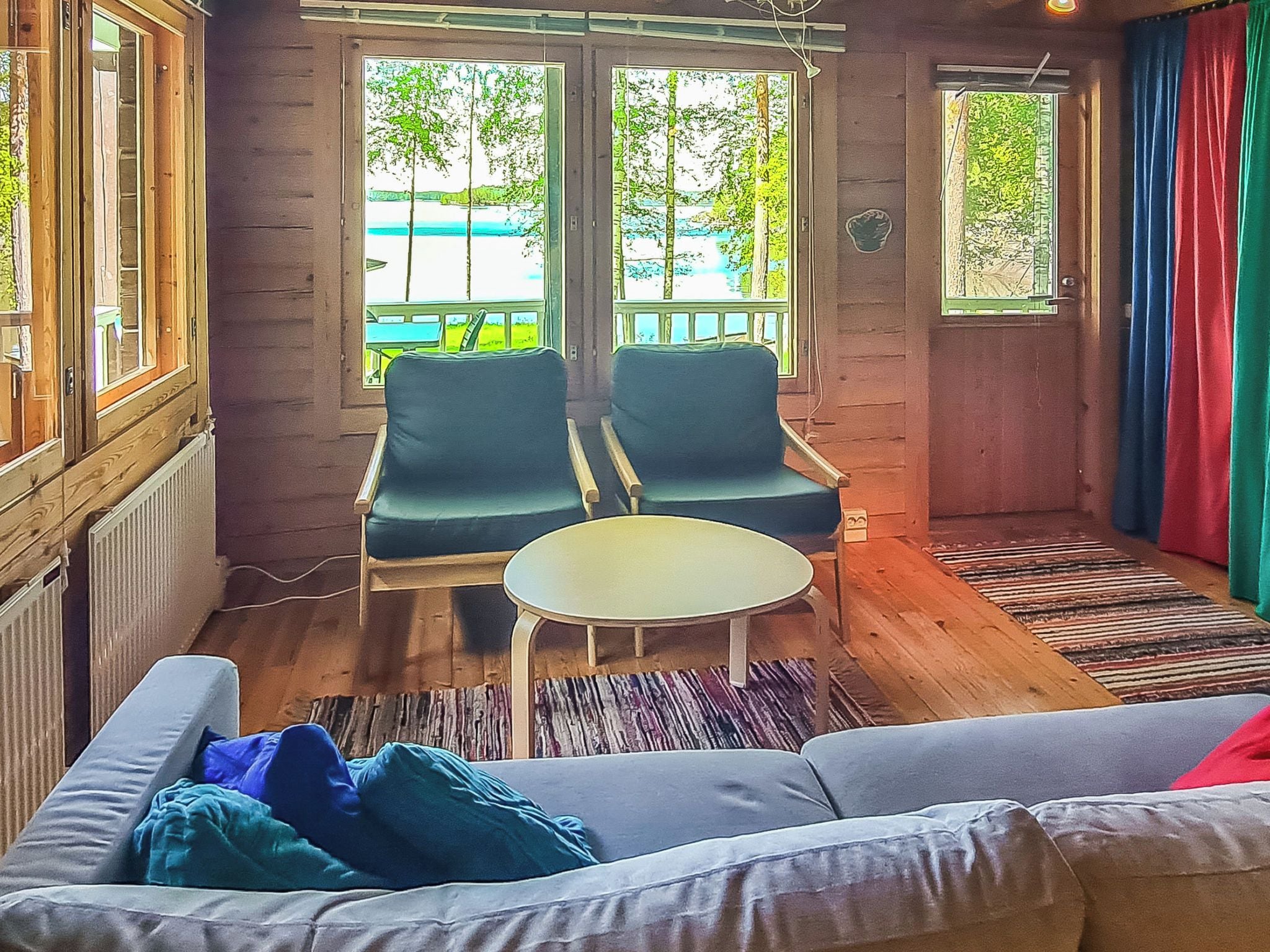 A room with a sofa, two armchairs, a small table, and a view of a beach through large windows.