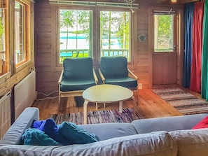 Une pièce comprenant un canapé, deux fauteuils, une petite table et donnant sur une plage grâce à de grandes fenêtres.