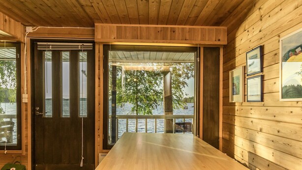 Une cabane en bois avec une grande table à manger, une porte donnant sur l’extérieur et des tableaux encadrés accrochés au mur.