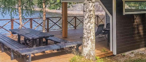 A wooden deck with picnic tables and a covered seating area by a body of water.