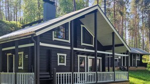 Une cabane en rondins à deux étages, dotée d’un porche et de balustrades blanches, entourée d’une forêt.