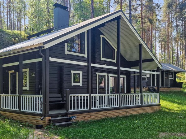 A two-story log cabin with a porch and white railings, surrounded by a forest. - Kiviranta by Interhome (Savonlinna)